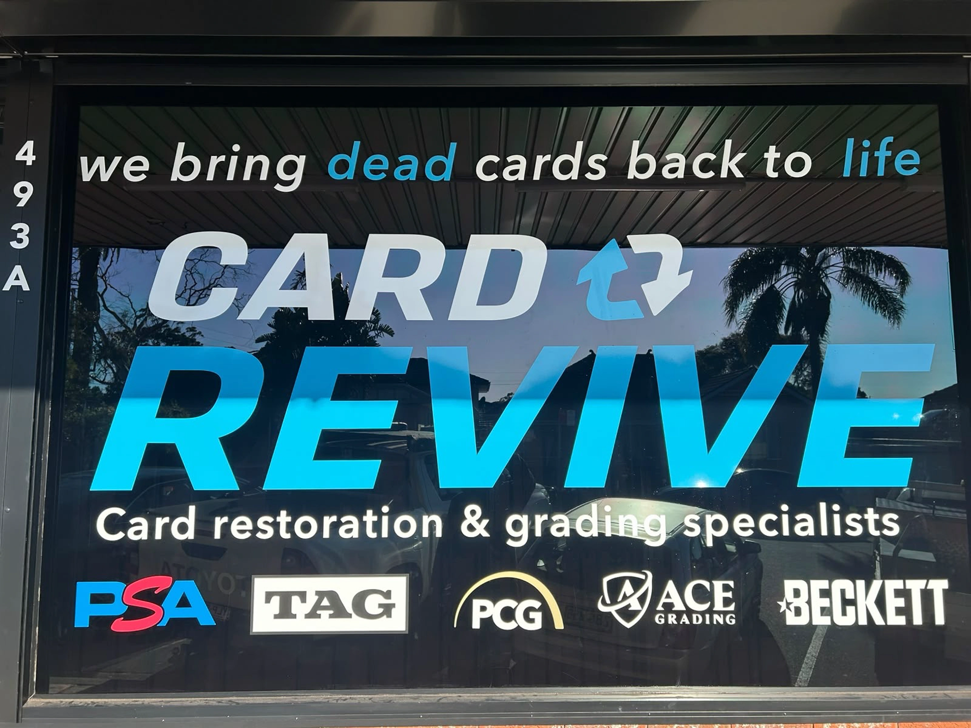 Close view of the CardRevive storefront window with the Card Revive name and grading-service logos.