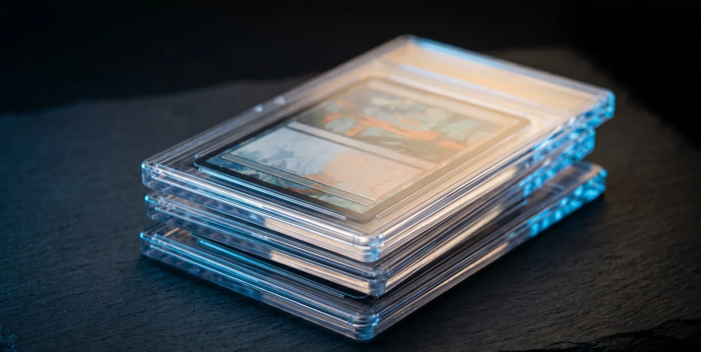 Stacked acrylic graded card slabs on dark slate, lit with cool blue rim light