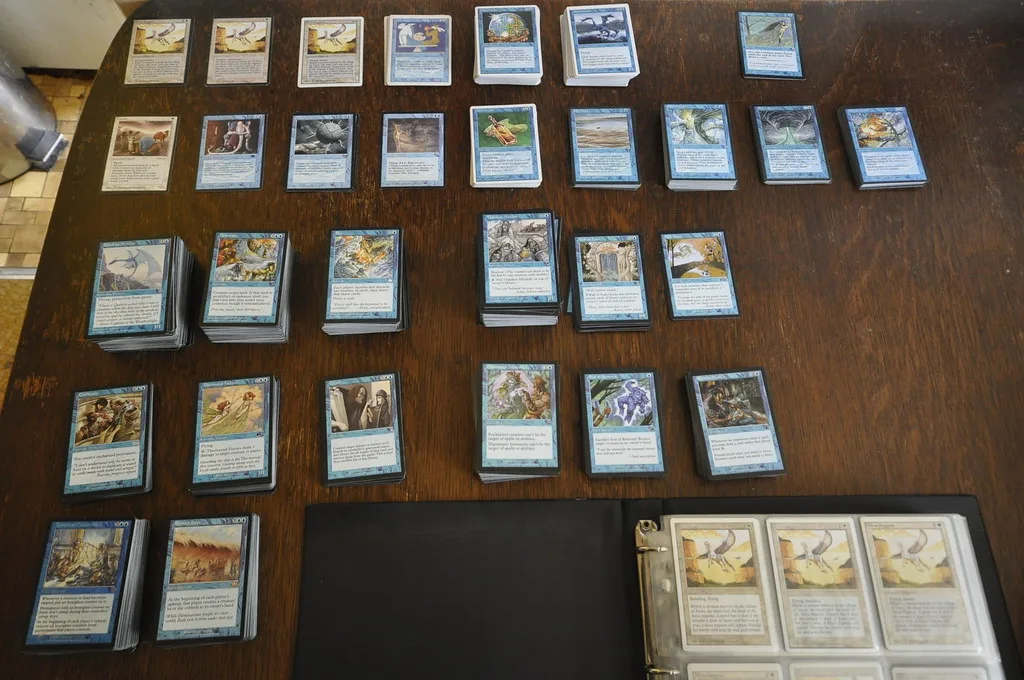 A Magic: The Gathering collection sorted into stacks on a table beside an open card binder.