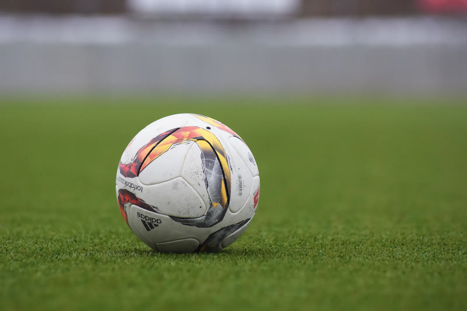 A weathered white, red and yellow soccer ball resting on a grass pitch.