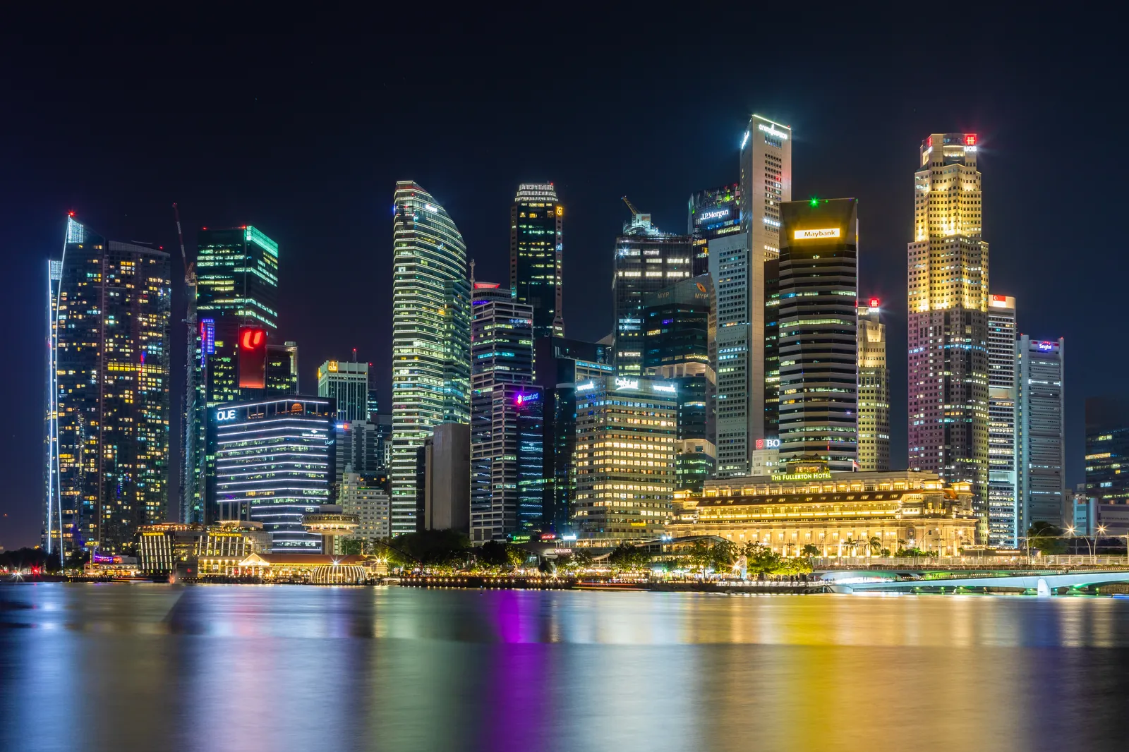 The illuminated Singapore skyline and Marina Bay waterfront reflected in the water at night.