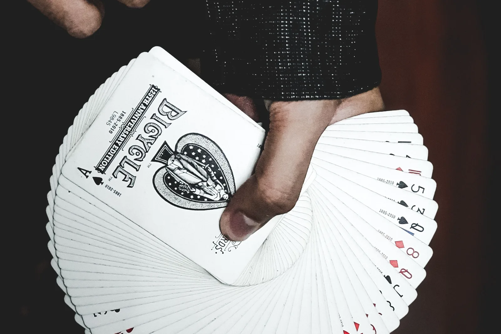 A hand fans out a full deck of playing cards, showing the faces of several number and face cards.