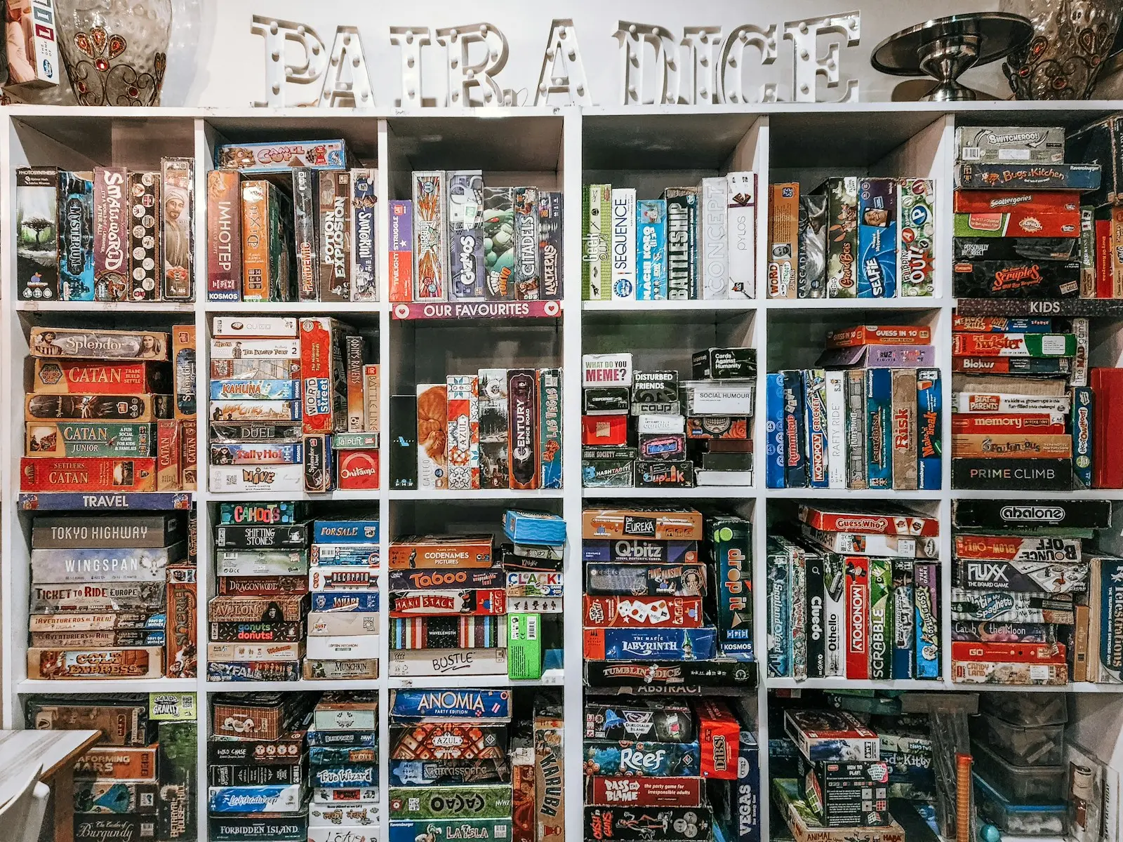 Floor-to-ceiling white shelves packed with boxed tabletop games at a game cafe.