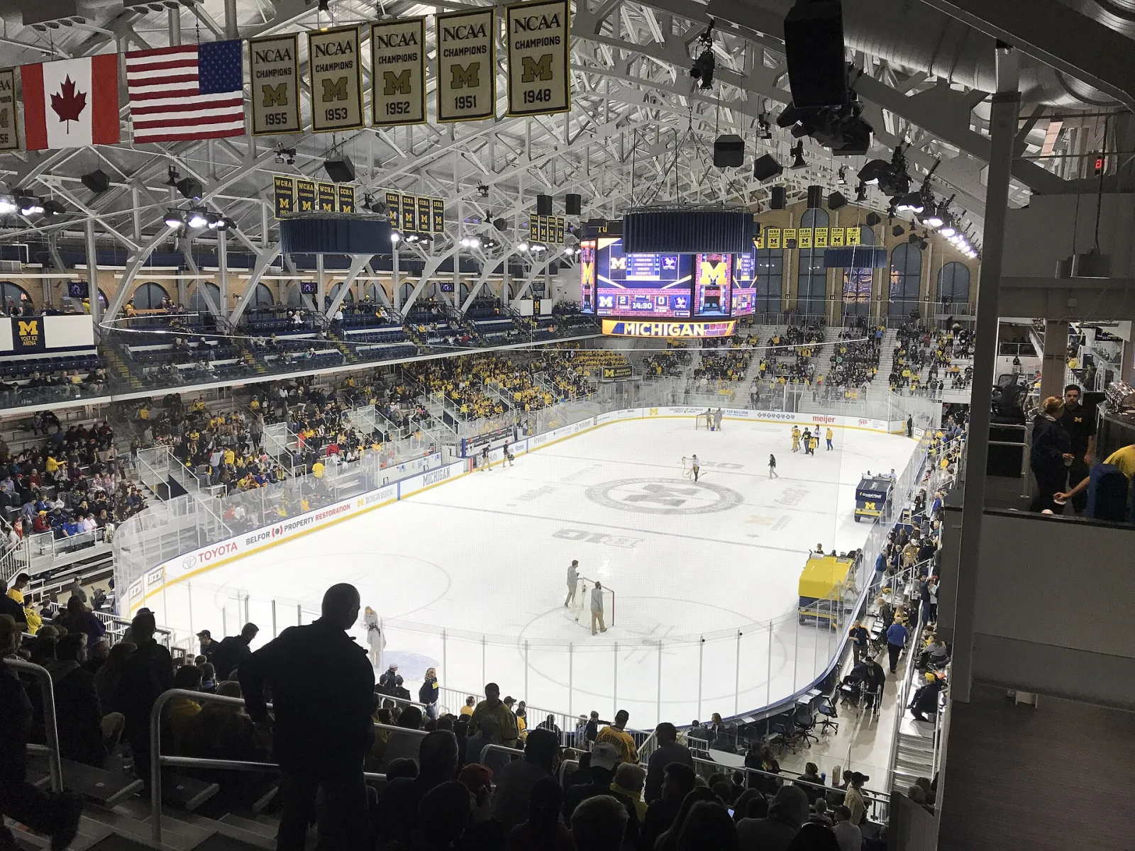 A packed indoor ice hockey arena seen from the upper stands during intermission, with championship banners hanging from the roof.