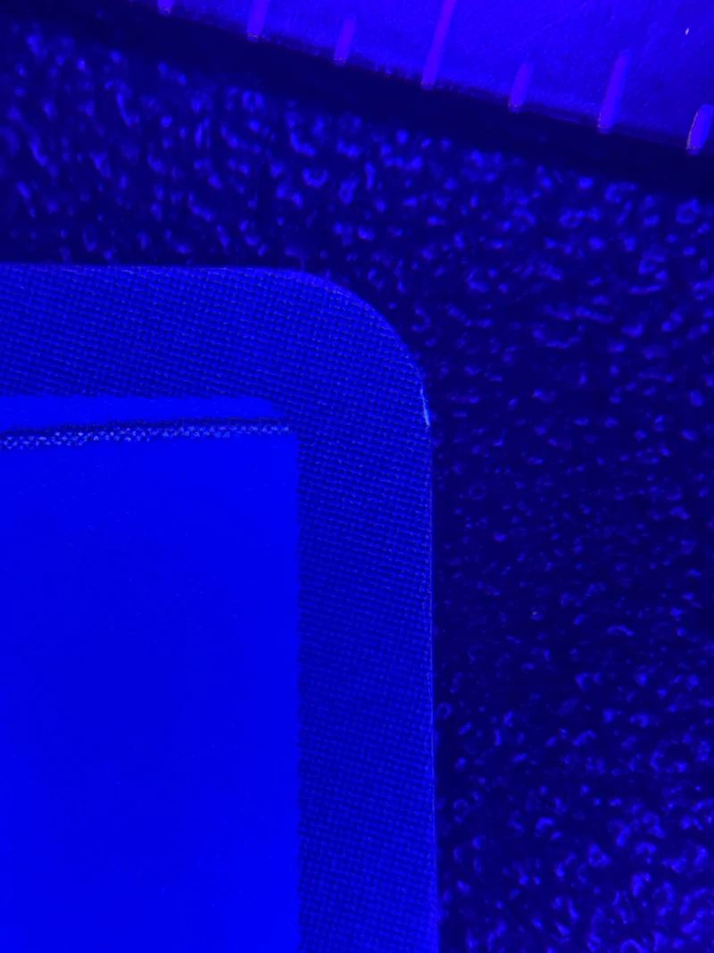 The top-right corner of the Nami OP01-016 card back under blue LED magnification at intake inspection, before corner correction, surface texture visible with a measurement scale across the top of the frame