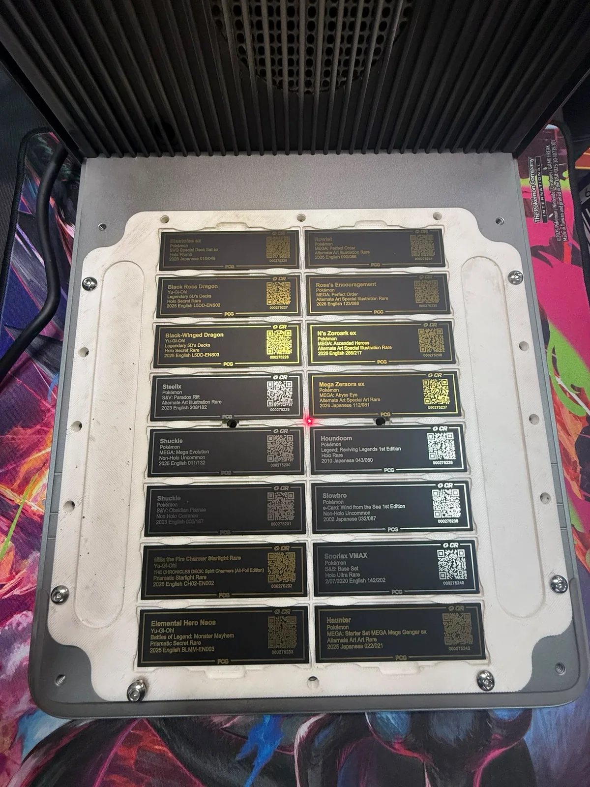 Freshly made black and gold PCG rear labels arranged in a production fixture, with the CardRevive CR mark printed above certification QR codes on multiple labels